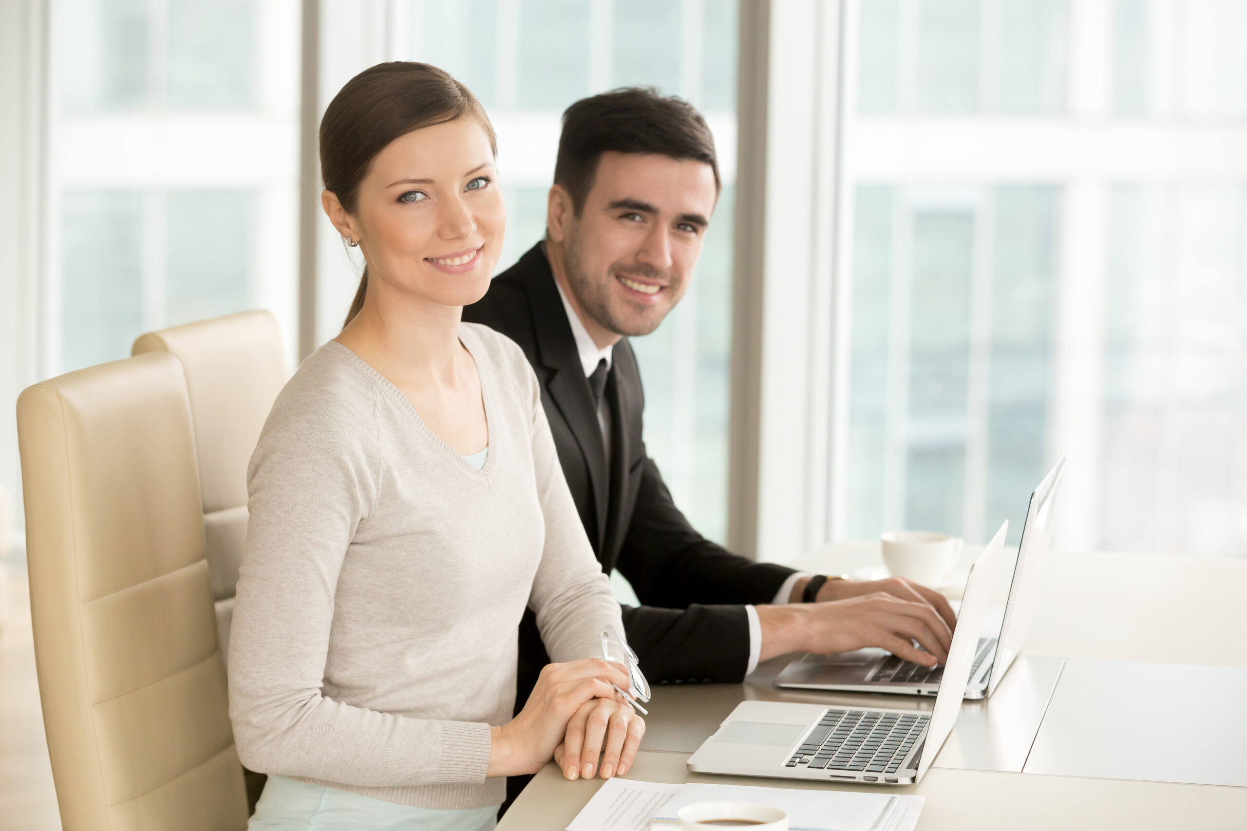 Smiling professional businesswoman and businessman looking at camera, leaders posing with laptops at desk, executive team portrait, internet marketing, corporate education, online business concept